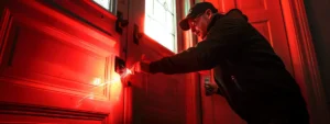 a locksmith in action, skillfully picking a lock on a red door during an emergency lockout situation.